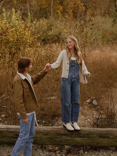 two people standing on a log in the woods holding hands and smiling at each other