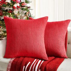 two red pillows sitting on top of a couch next to a christmas tree