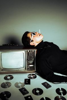 a man laying on top of a table next to an old fashioned tv and cd's