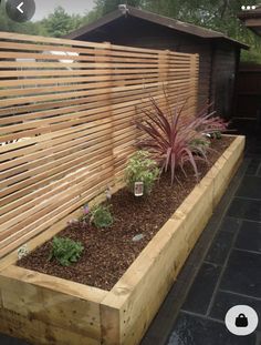 a wooden planter filled with lots of plants next to a fenced in area