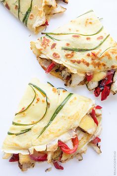 three quesadillas are cut in half on a white surface with green and red toppings