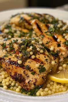 a white plate topped with chicken and garnished with green herbs next to a slice of lemon