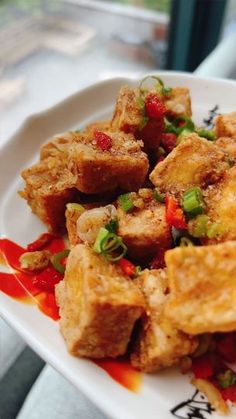 a white plate topped with tofu covered in sauce and green onions next to a window