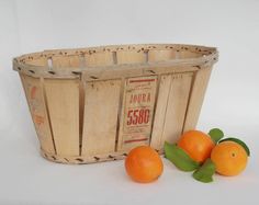 three oranges in a wooden basket next to some leaves