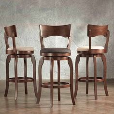 three wooden stools with leather upholstered seats in front of a concrete wall