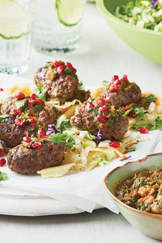 some meatballs are sitting on a plate next to a bowl of salad and a glass of water