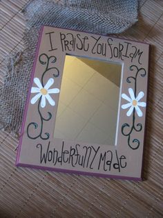 a mirror that is sitting on top of a wooden table with writing on it and flowers in the frame