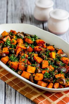 a white dish filled with cooked sweet potatoes and parsley on top of a wooden table