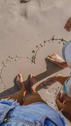 two people sitting on the beach writing in the sand with their feet up and heart drawn in the sand