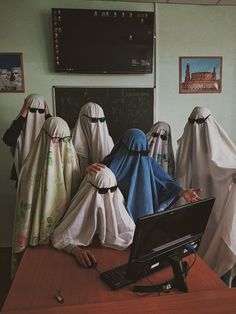 several people dressed in white and blue robes are sitting at a desk with a computer