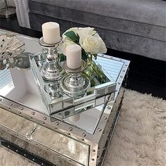 a mirrored coffee table with candles and flowers on it in front of a gray couch