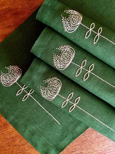 three green napkins with embroidered designs on them sitting on a wooden table next to each other