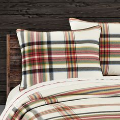 a bed with plaid sheets and pillows on top of it in a wooden headboard