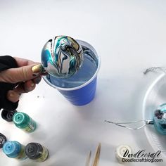 someone is painting an ornament on the side of a cup with blue and white paint