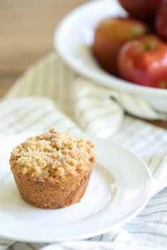 a muffin on a plate with apples in the background