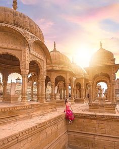 a woman sitting on top of a stone wall in front of a building with arches and pillars