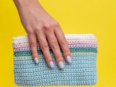 a woman's hand holding a crocheted clutch bag on a yellow background