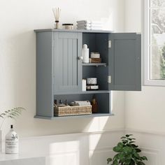 a gray cabinet with shelves and baskets on it next to a potted plant in a white room