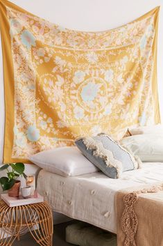 a yellow tapestry hanging over a bed with pillows and blankets on top of it in a bedroom