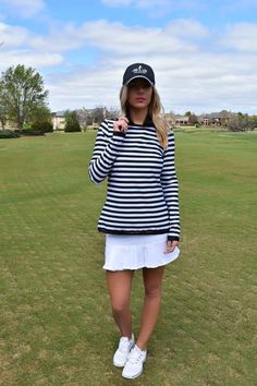 a woman standing on top of a green field wearing a black and white striped shirt