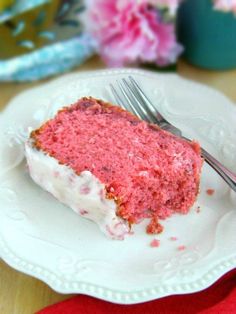 a piece of cake on a white plate with a fork and pink flowers in the background