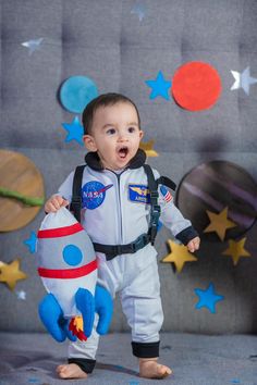 a baby boy in an astronaut suit holding a stuffed toy