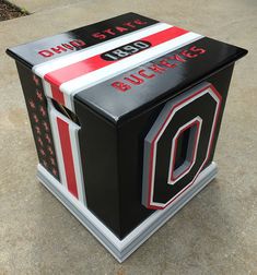 a black and red box with the letter o on it's side sitting on concrete