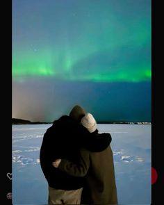 two people standing in the snow looking at an aurora bore