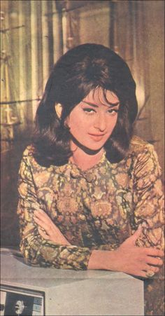 an old photo of a woman sitting at a table with her arms crossed and looking off to the side