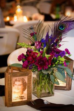 a vase filled with purple flowers next to a framed photo on a table in front of candles