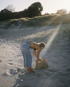 a woman bending over in the sand with a bag