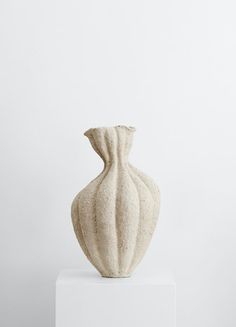 a large white vase sitting on top of a white pedestal in front of a wall