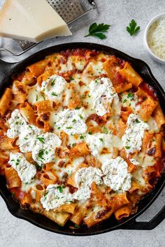 a skillet filled with pasta, cheese and parmesan on top of a table