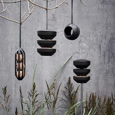 three black hanging pots filled with food next to a tree and planter in front of a concrete wall