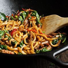 a wok filled with noodles and vegetables on top of a wooden table