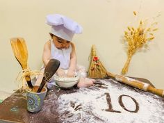 a young child sitting on top of a wooden table with flour and utensils