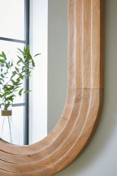 a wooden mirror hanging on the wall next to a potted plant in front of a window