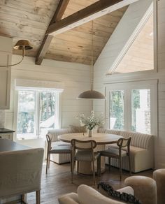 a living room with white walls and wooden ceilings, two couches and a round dining table