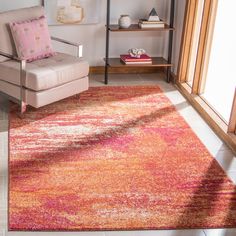 an orange and pink rug in a living room with a chair, bookshelf and window