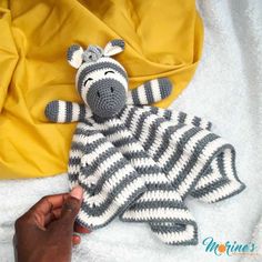 a hand holding a knitted zebra laying on top of a bed next to a yellow blanket