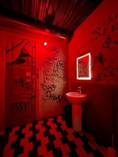 a bathroom with red walls and black and white checkered flooring, graffiti on the walls