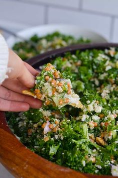 a person holding a piece of food over a salad in a wooden bowl on a table