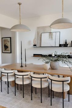 a dining room table surrounded by white chairs and hanging lights over it's head