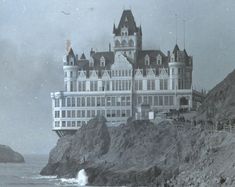 an old black and white photo of a large building on top of a cliff next to the ocean