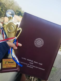 a person holding up a trophy and a book in their hand with ribbons around it