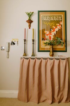 an old fashioned poster hangs on the wall above a table with candles and vases