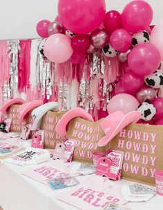 a table with pink and white balloons, cowgirl decorations and other items on it