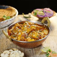 some food is in a metal bowl on a wooden table with other dishes around it