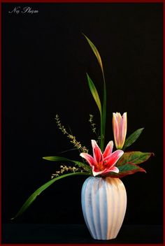 a white vase filled with flowers on top of a black table next to a red frame