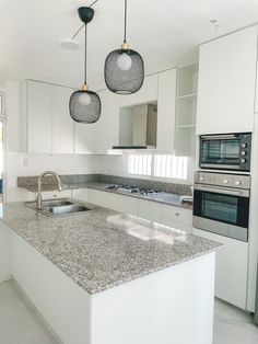 a kitchen with white cabinets and granite counter tops, two ovens and an island